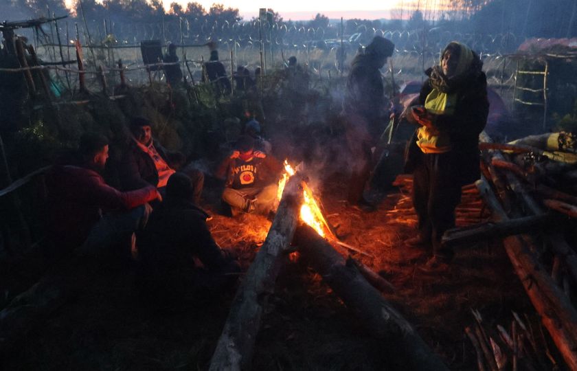 Migranty se ohřívají u ohně v táboře na bělorusko-polské hranici v oblasti Grodno. Foto: Profimedia