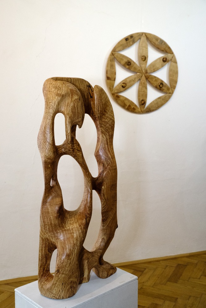 Foto z výstavy Martina Patřičného: socha Pozdrav, bukové dřevo, a reliéf Květ života, rovněž buk.